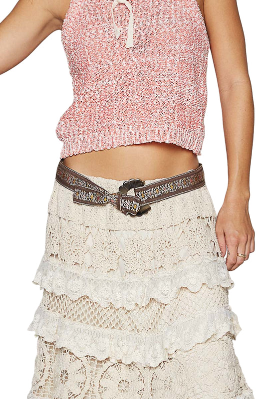 Person wearing a pink textured top and white lace skirt with a brown belt.