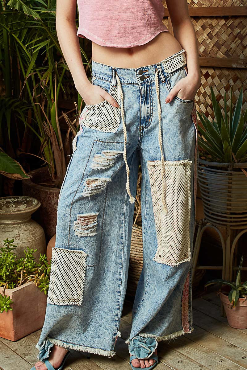 Person wearing patchwork jeans with a pink top in a garden setting
