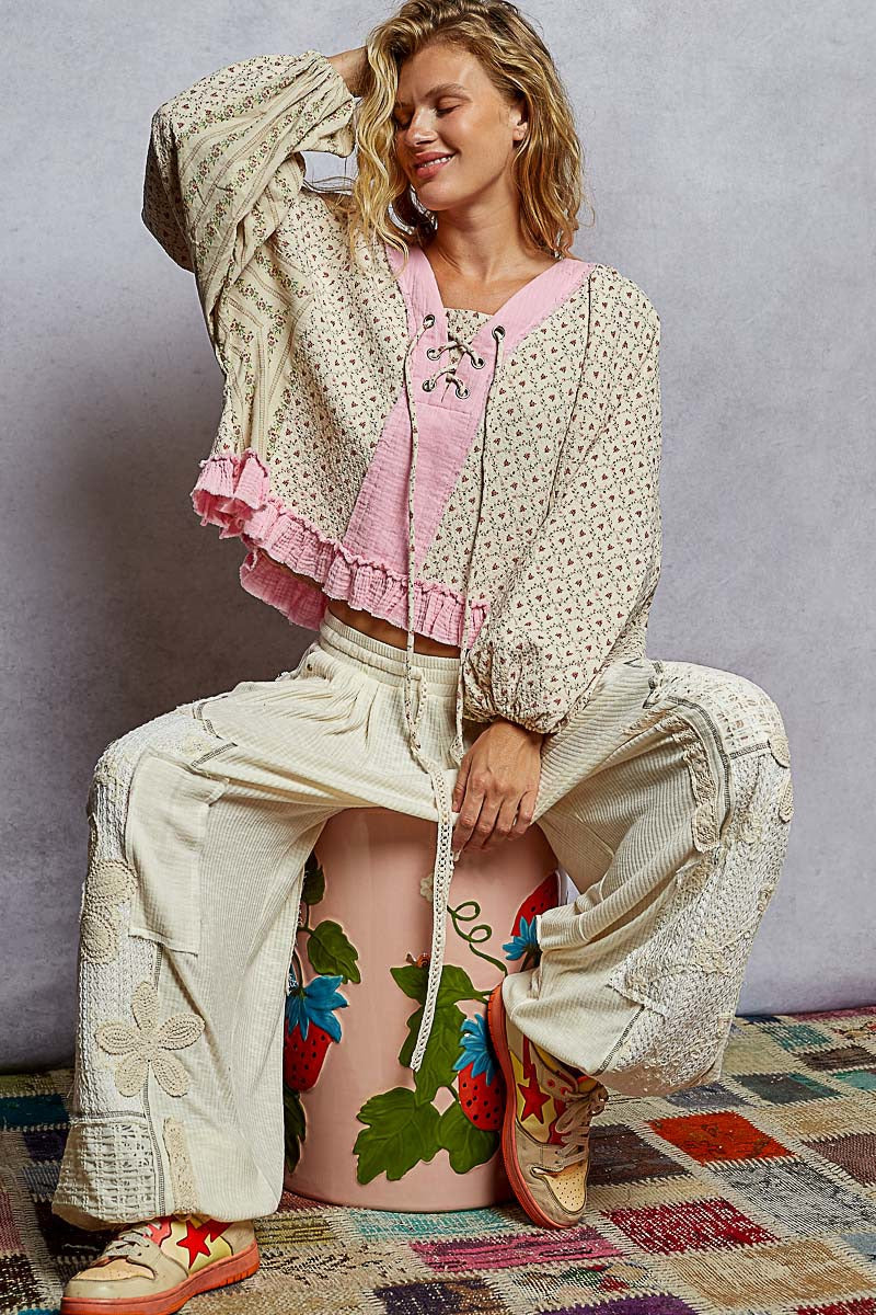 Woman wearing a patterned outfit with a pink top and beige pants, sitting on a colorful rug.