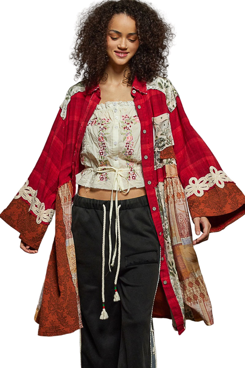 Woman wearing a red and patterned long coat over a white embroidered top and black pants on a white background