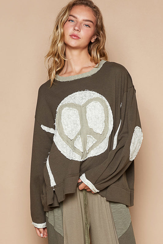 a woman standing in front of a wall wearing a peace sign sweater