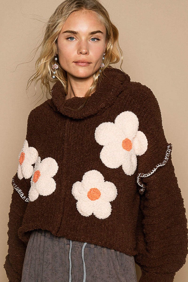 a woman wearing a brown sweater with white flowers on it