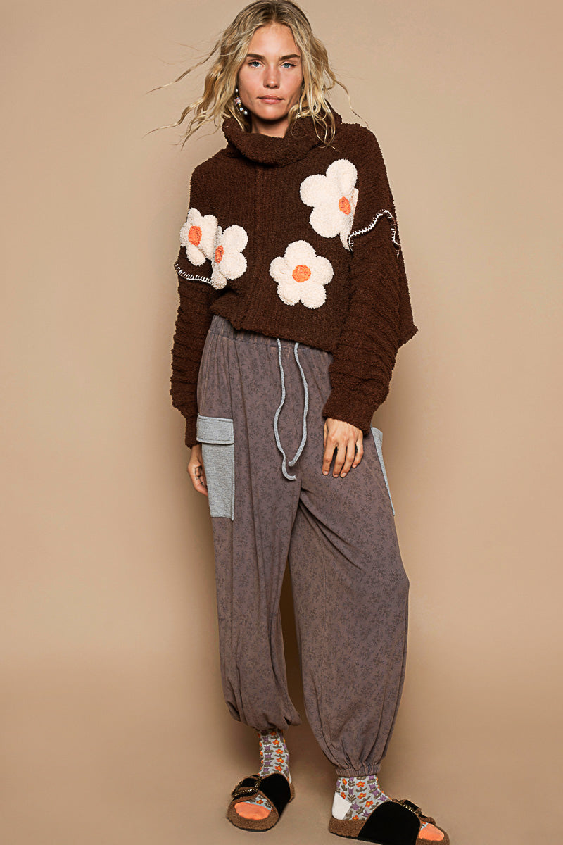 a woman standing in front of a wall wearing a sweater with flowers on it