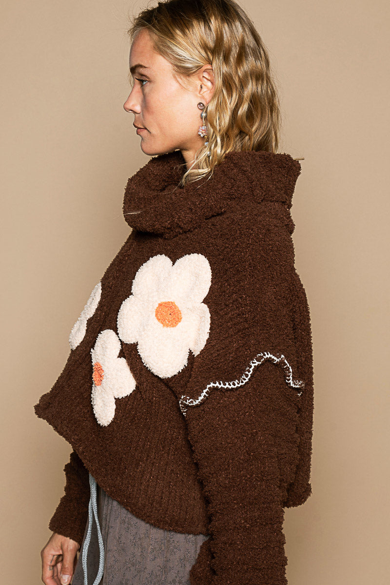 a woman wearing a brown sweater with a flower on it