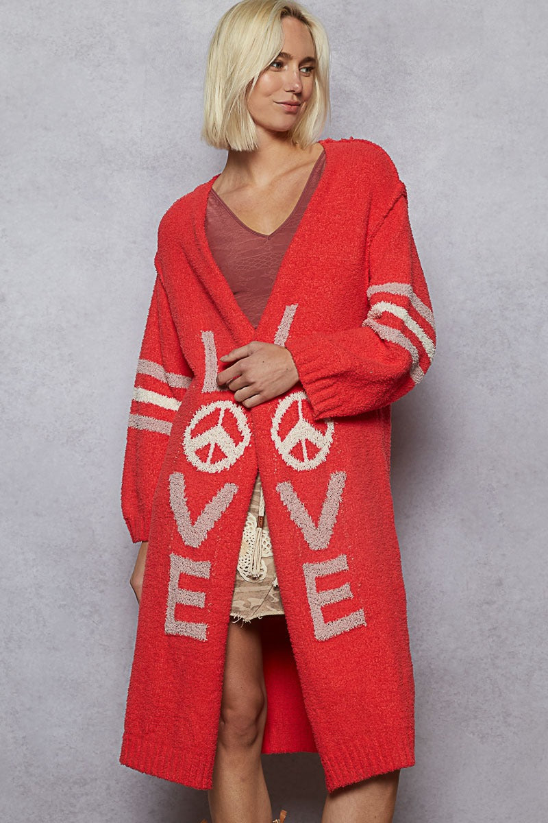 Woman wearing a red cardigan with 'LOVE' and peace signs on a gray background