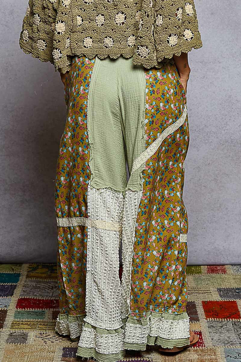 Person wearing a traditional outfit with a floral patterned dupatta, green top, and white pants on a textured floor.