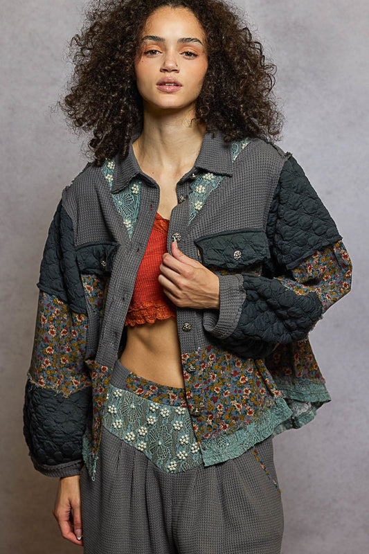 Woman wearing a layered outfit with a floral shirt and quilted jacket against a gray background