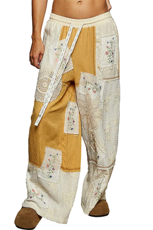 Patchwork pants with floral embroidery on a textured floor.