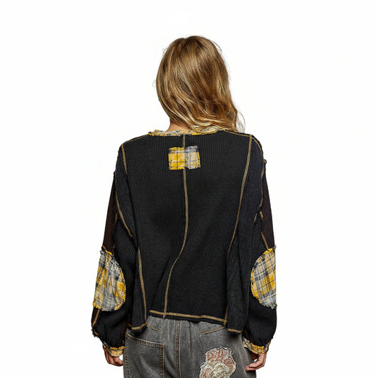 Person wearing a black jacket with yellow and white patchwork details on a gray background