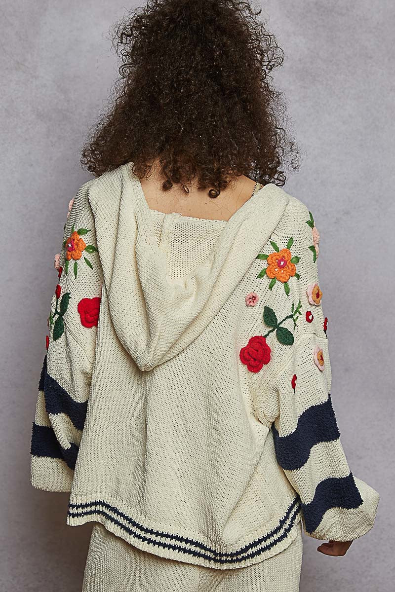 Person wearing a cream-colored hoodie with floral embroidery on a gray background
