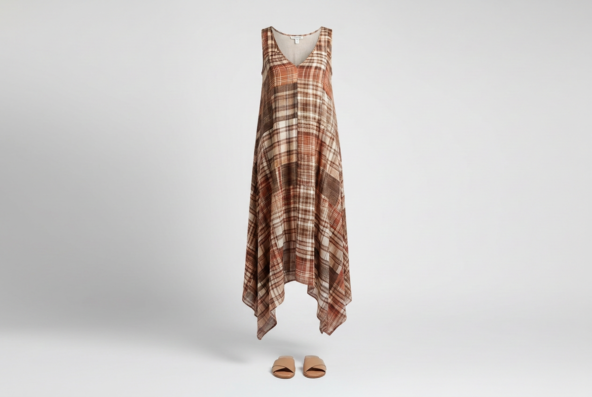 Brown and cream plaid sleeveless maxi dress with a handkerchief hem and tan slides against a softly shaded gray backdrop.