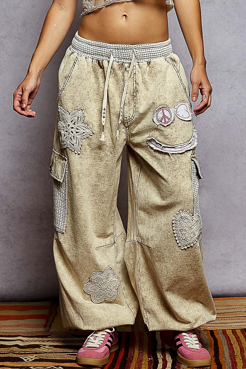 Person wearing beige patchwork pants with decorative elements on a plain background