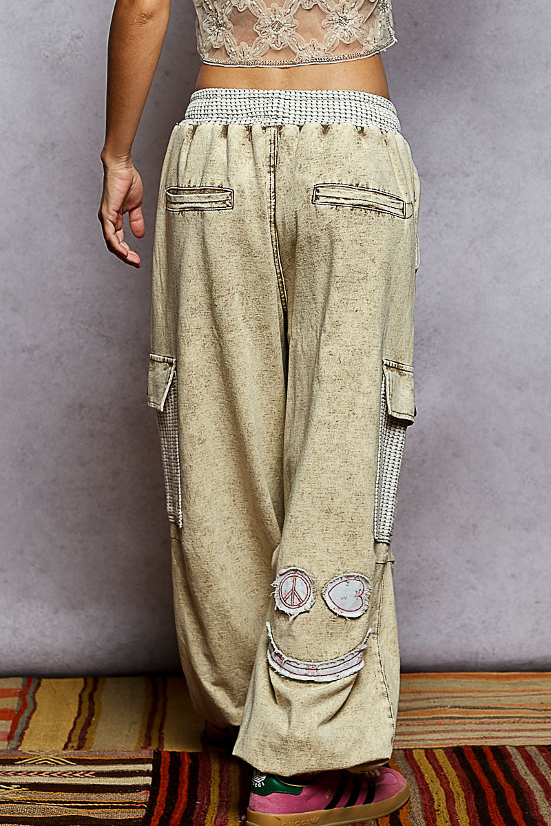 Beige cargo pants with peace sign patches worn by a person against a gray wall.