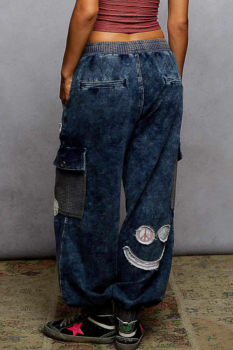 Person wearing blue denim cargo pants with patches against a gray background