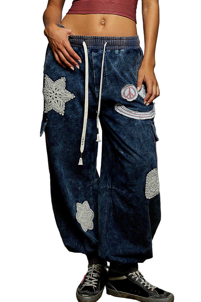 Person wearing dark blue patchwork pants with decorative elements on a plain background