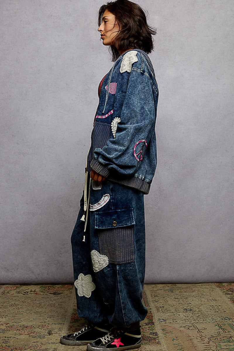 Person wearing a long, patchwork denim coat against a plain background