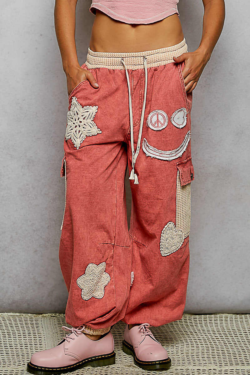 Person wearing pink pants with decorative patches against a gray background