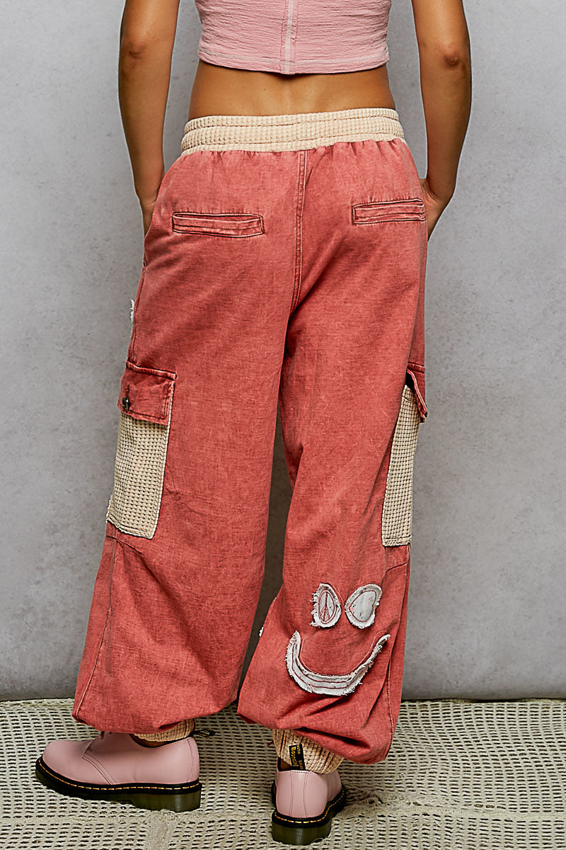 Person wearing pink cargo pants with smiley face design on a gray background