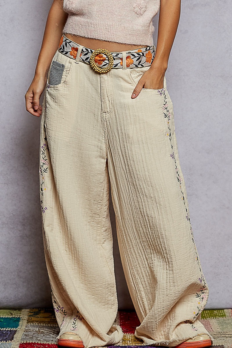 Beige wide-leg pants with floral patterns and a decorative belt on a plain background