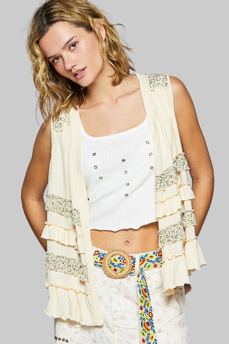 Woman wearing a white top and colorful skirt with an embellished beige cardigan on a gray background