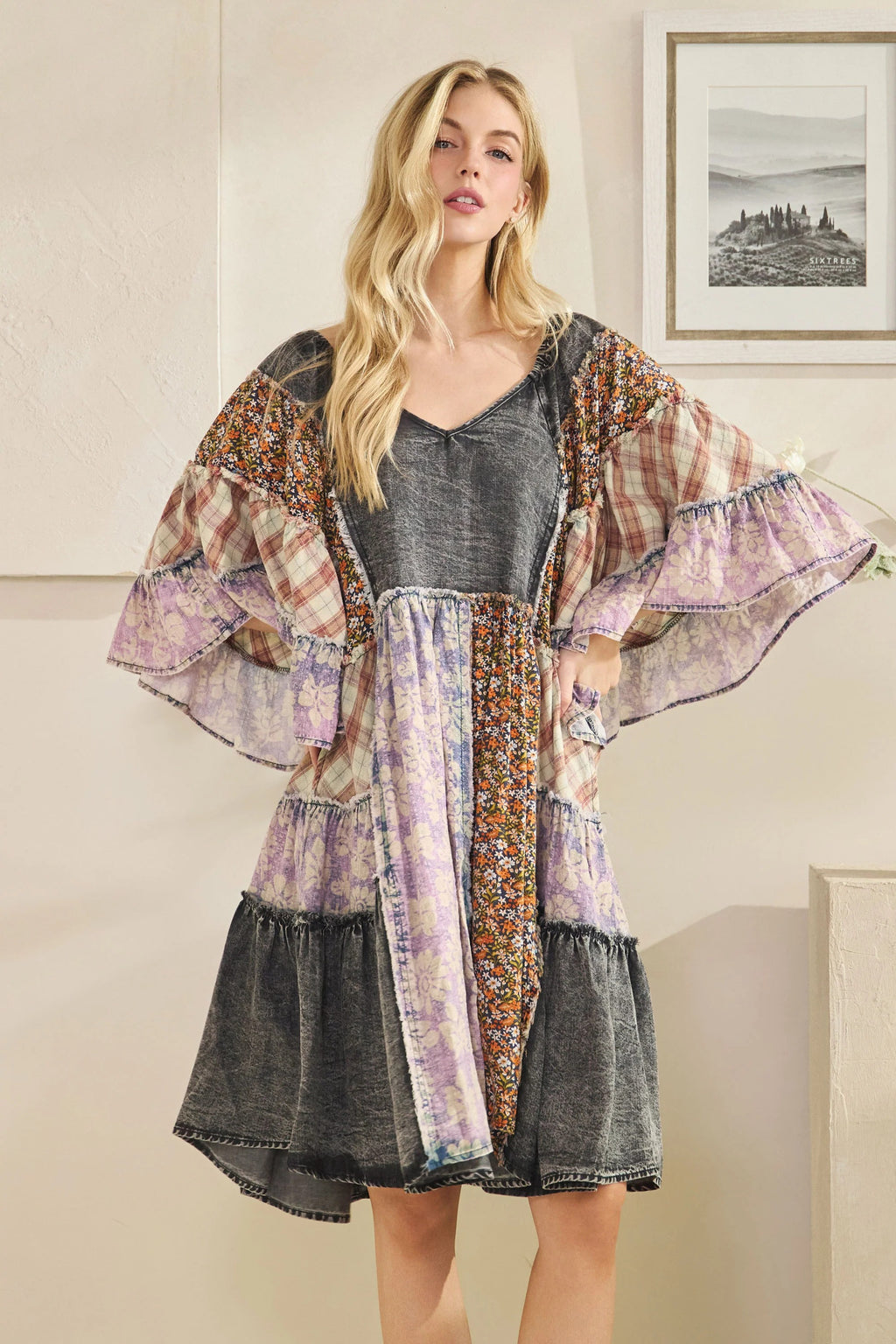 Woman wearing a patterned kimono-style jacket over a dress in a room with a painting on the wall.