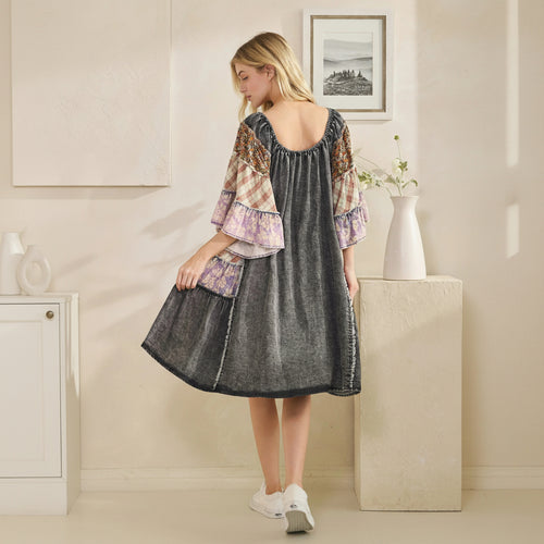 Woman wearing a patchwork dress in a room with a vase and framed picture on the wall.