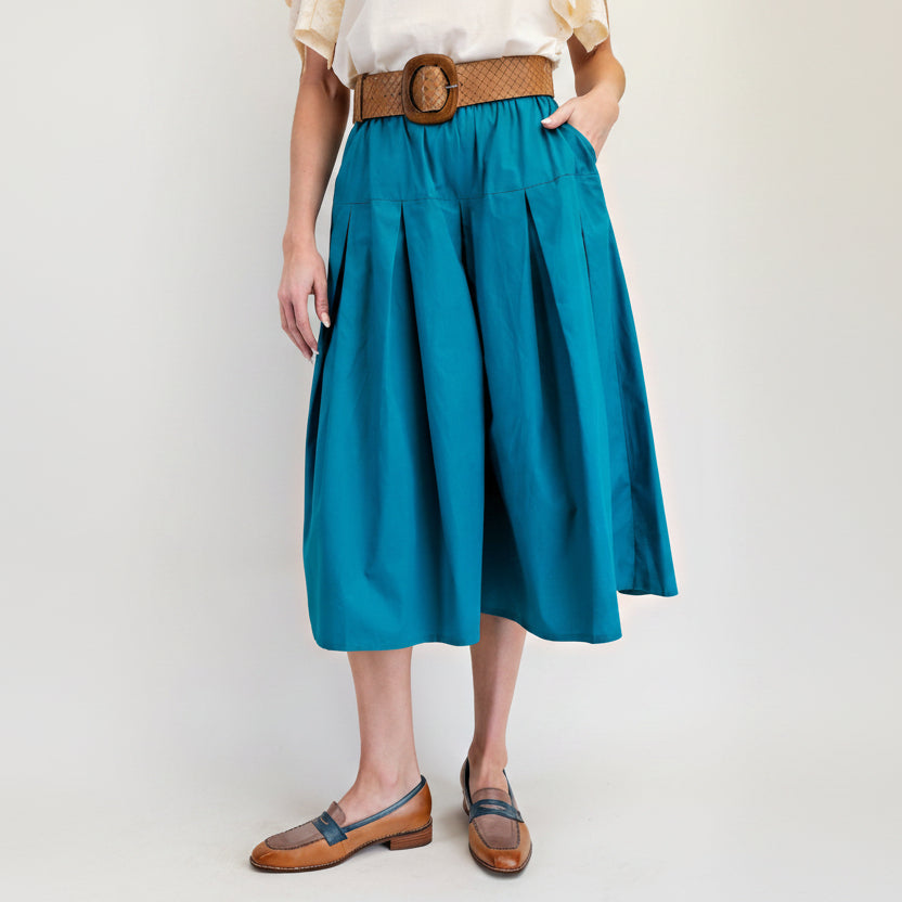 Easel teal cotton pleated midi skirt front close-up showing deep box pleats, side pockets, and woven belt
