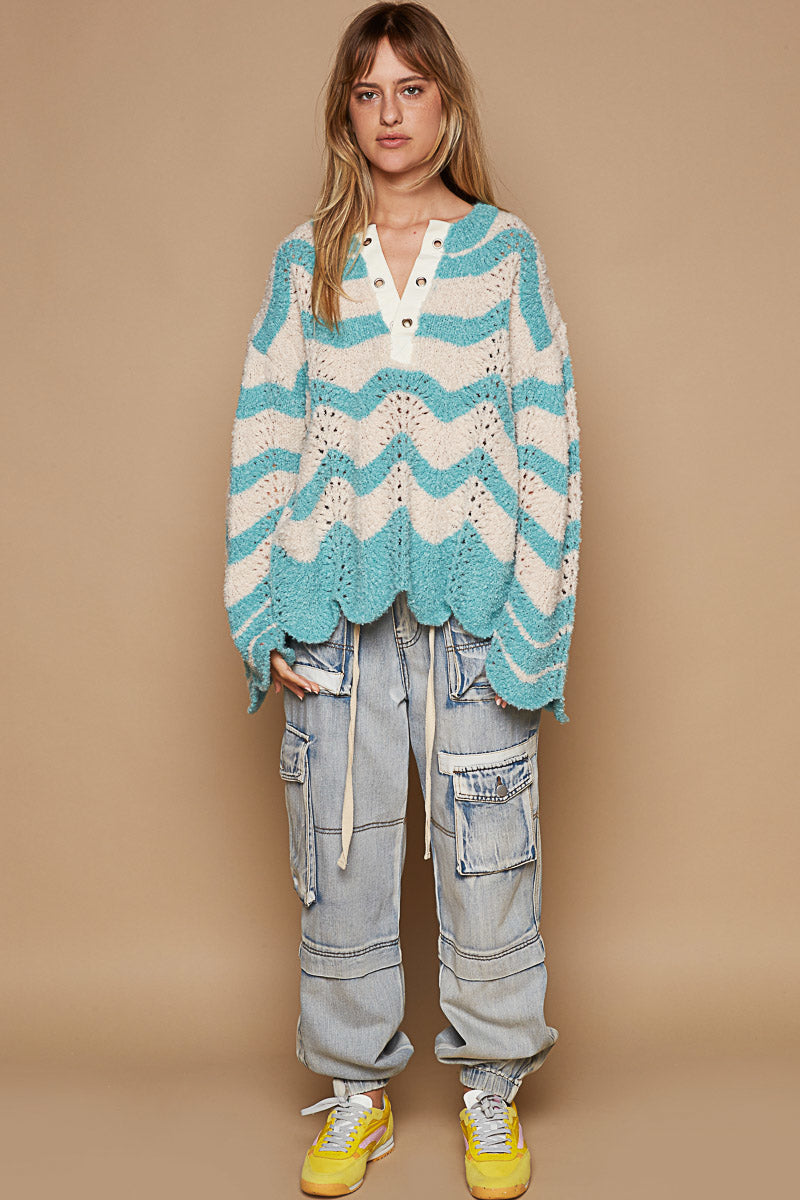 a woman standing in front of a wall wearing a blue and white sweater