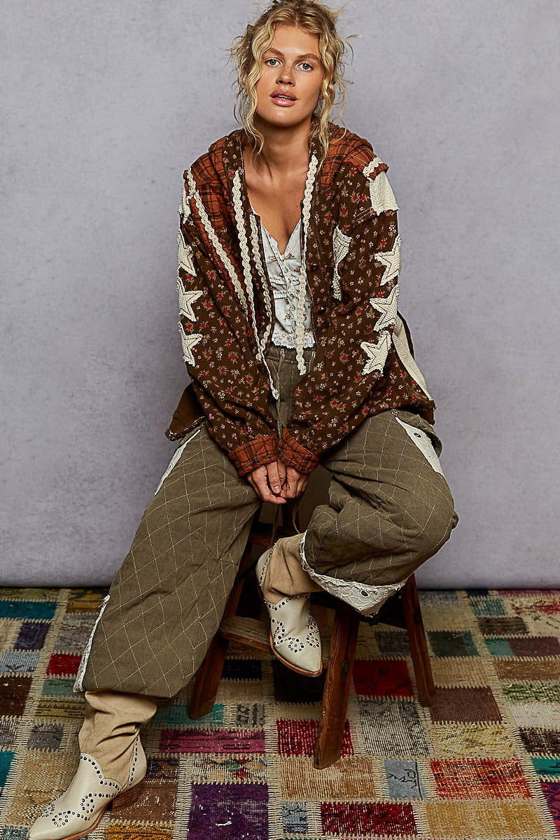Person wearing a patterned jacket and sitting on a stool against a plain background