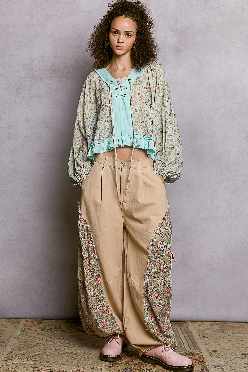 Woman wearing a floral blouse and beige pants against a plain background