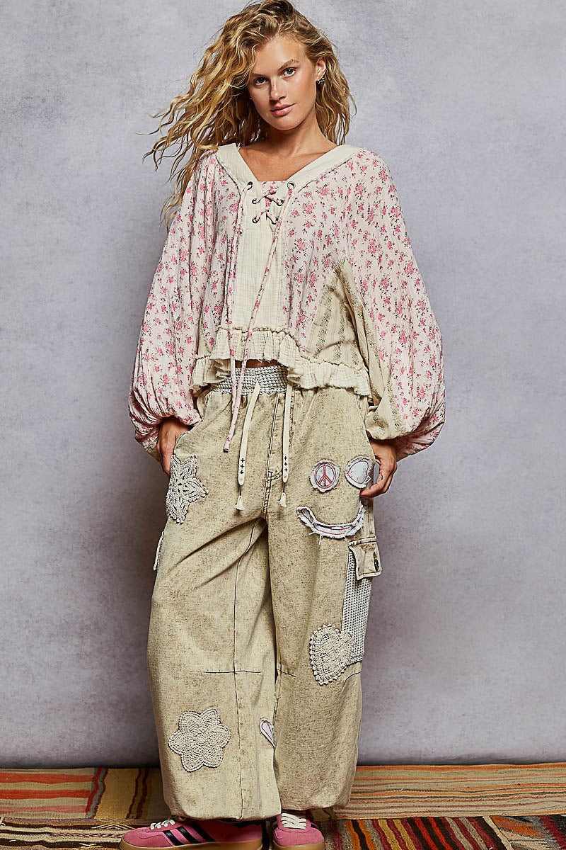Woman wearing a floral top and patchwork pants against a gray background