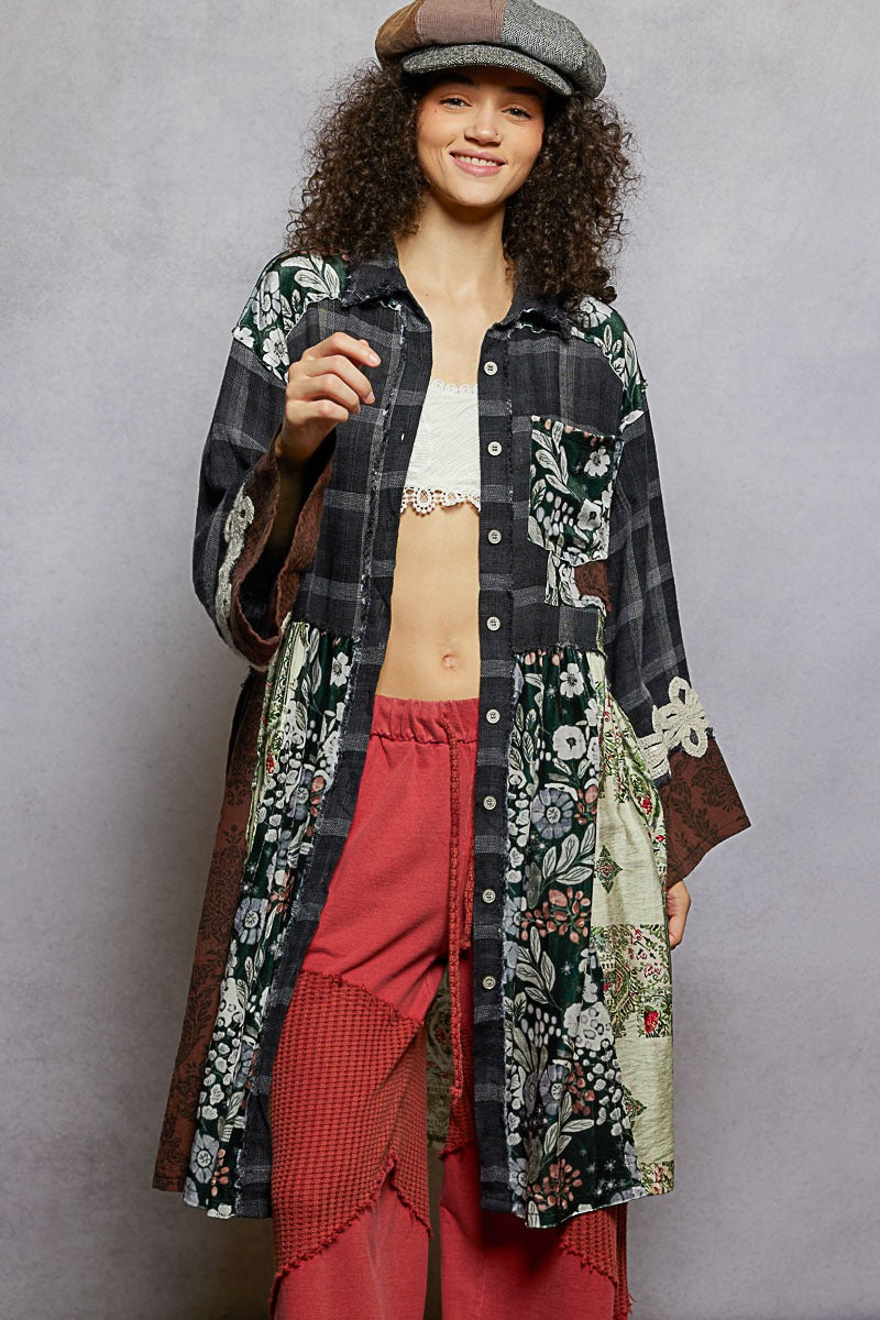 Person wearing a long, patterned coat over a white top and red pants against a gray background