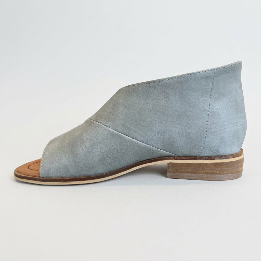 Light blue suede shoe with brown sole on a reflective surface