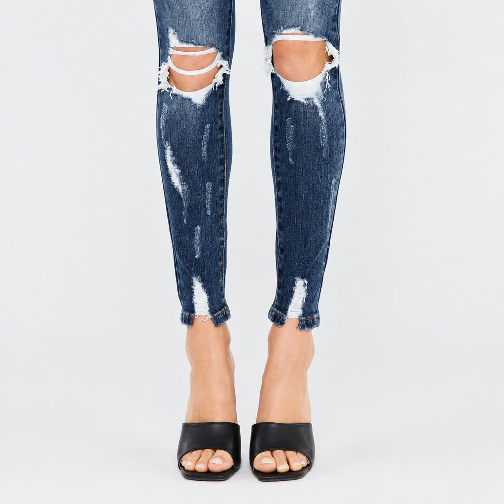 KanCan dark wash skinny jeans lower-leg close-up showing open knee rips and distressed stitched ankle hems