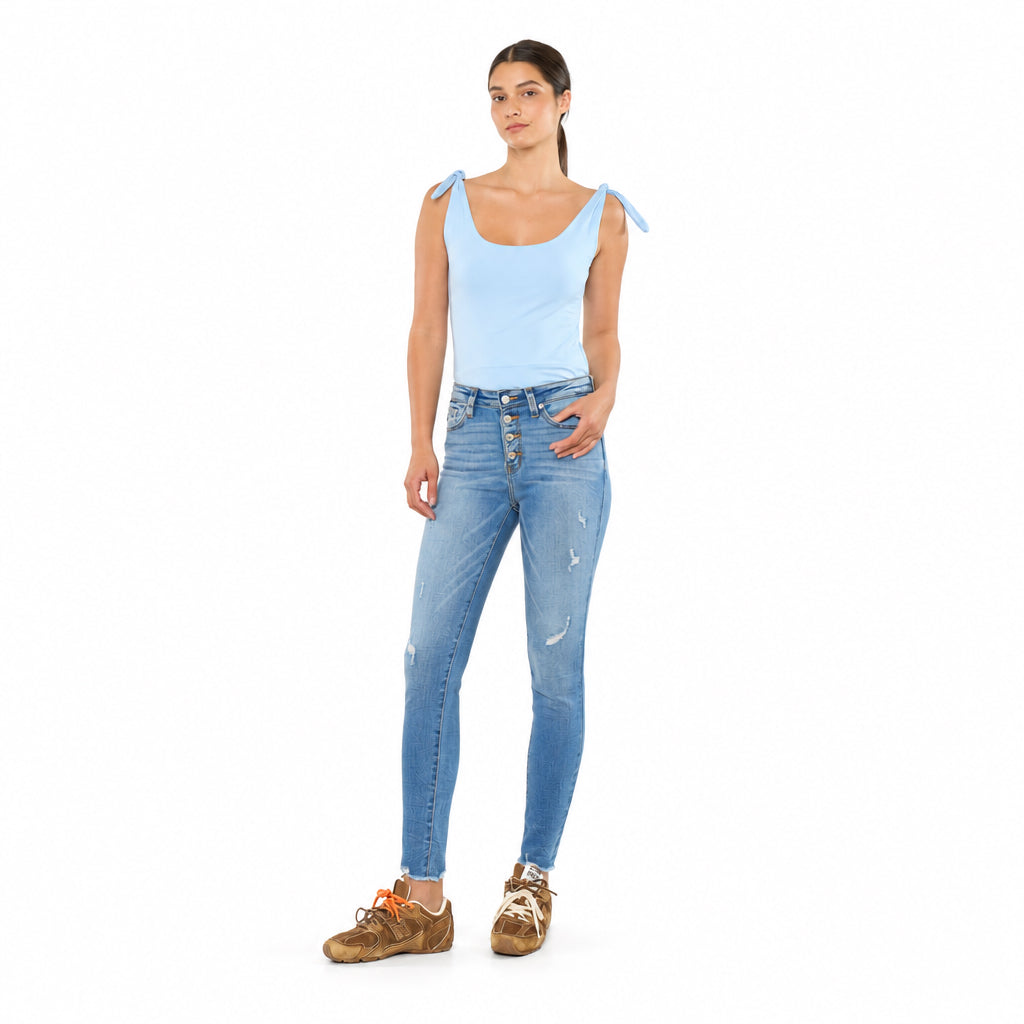 KanCan women's medium wash ankle skinny jeans, front view showing button fly and distressing with a light blue top