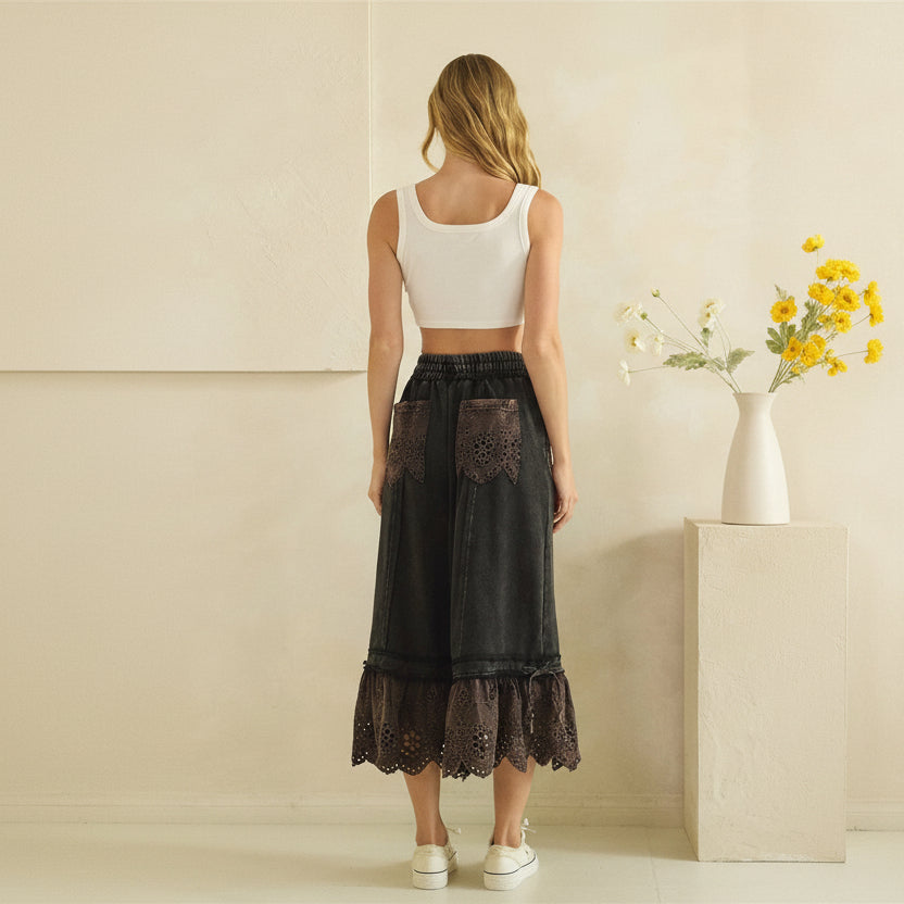 Oli & Hali black wide-leg pants on model, back view showing eyelet patch pockets and scalloped ruffle hem
