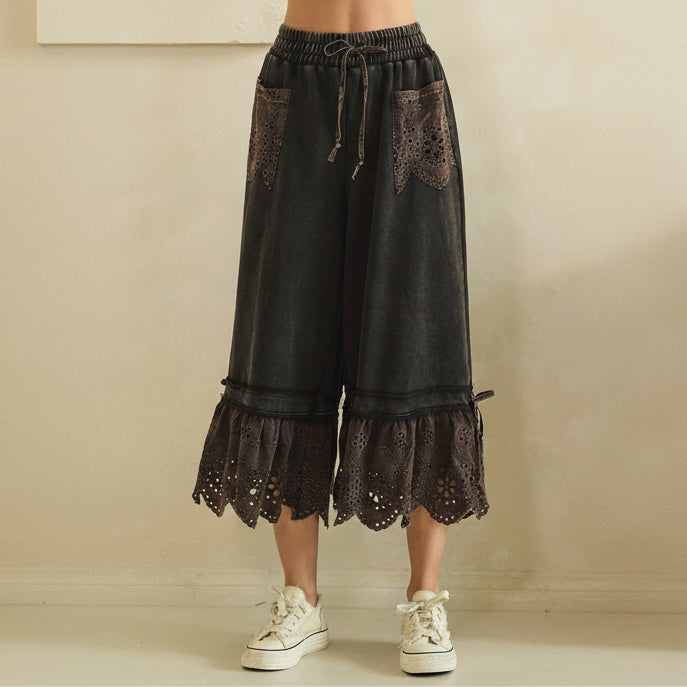 Close-up front crop of black mineral-wash wide-leg pants showing eyelet lace pockets and elastic drawstring waistband
