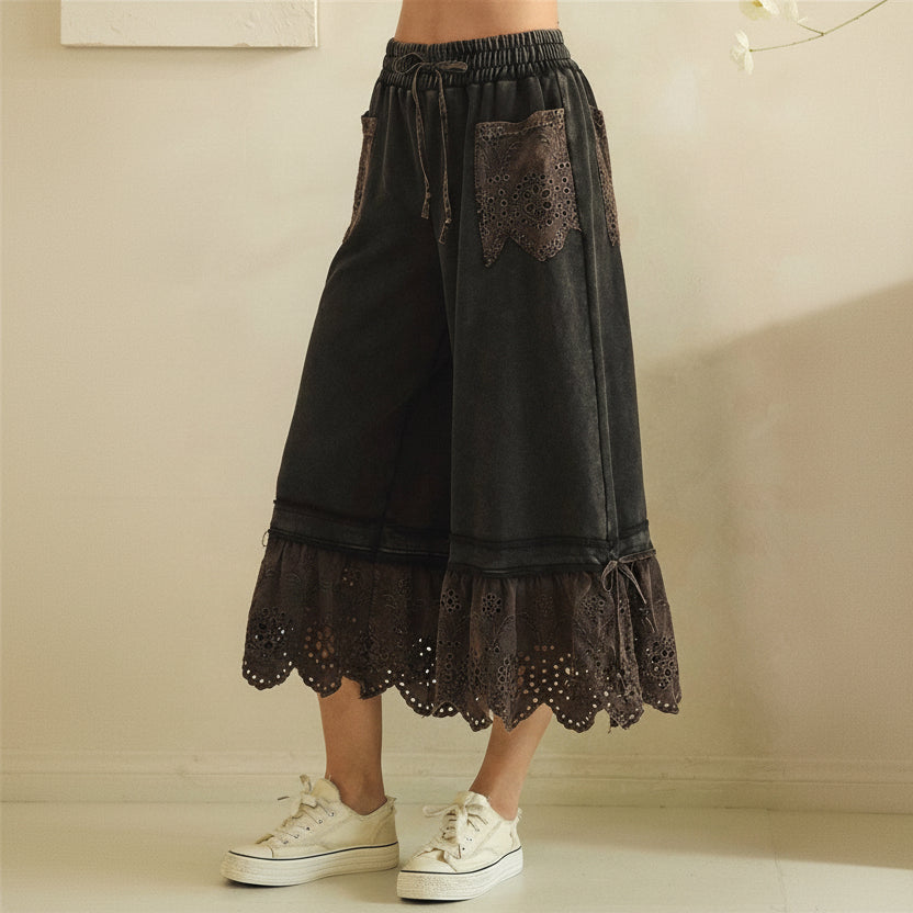 Close-up side view of black eyelet wide-leg pants showing waistband, eyelet pocket detail, and ankle tie
