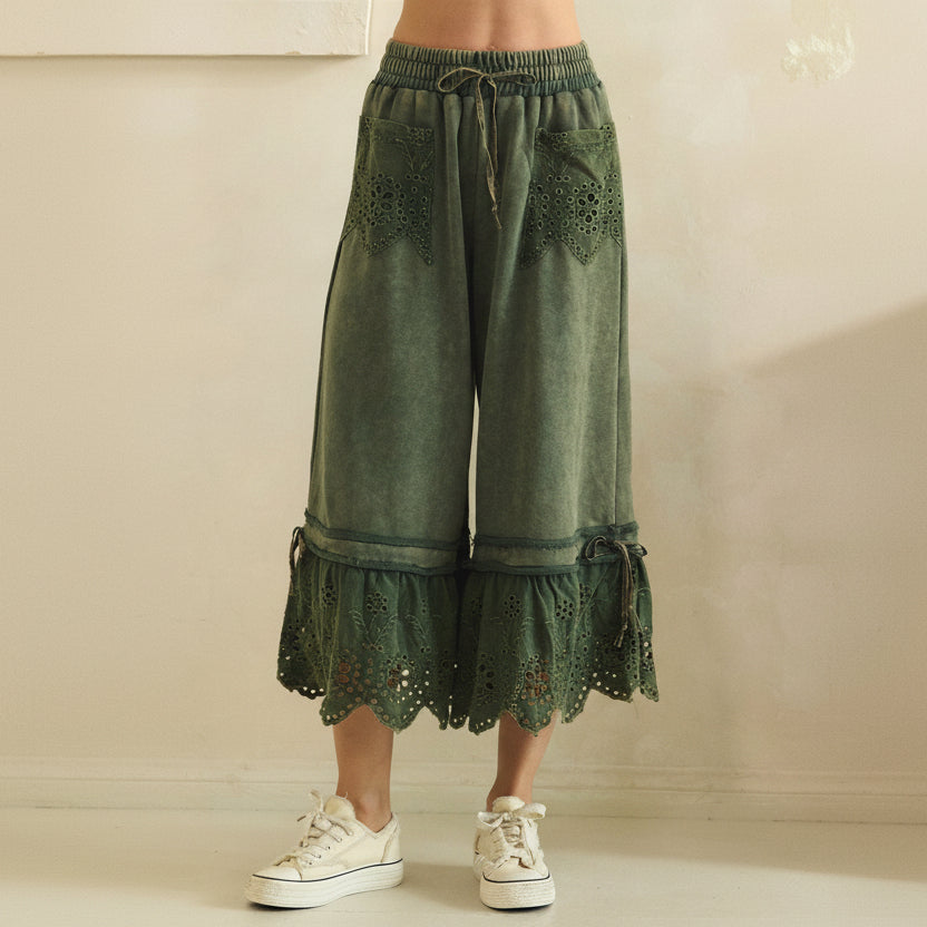 Close-up front crop of teal green mineral-wash wide-leg pants showing eyelet lace pockets and drawstring waist
