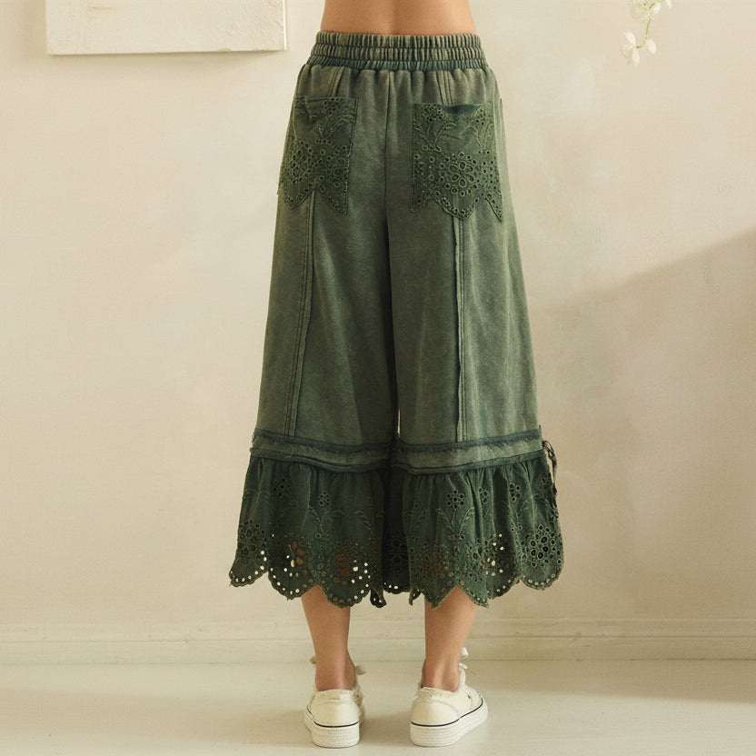 Close-up back view of teal green wide-leg pants showing eyelet patch pockets and scalloped ruffle hem
