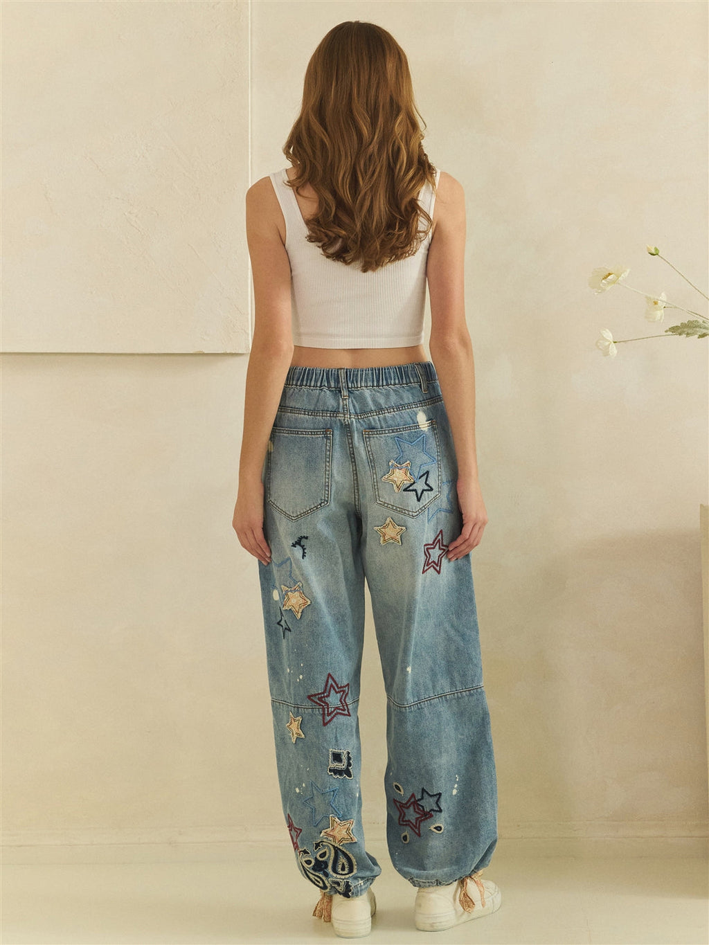 Rear full-length view of blue star embroidered jeans showing back pockets and gathered waistband