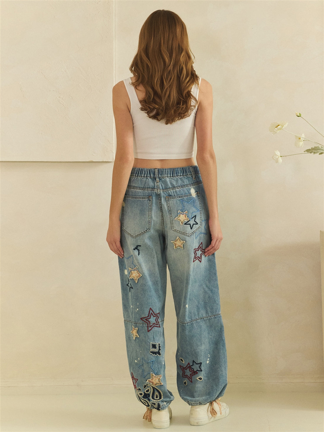 Rear full-length view of blue star embroidered jeans showing back pockets and gathered waistband
