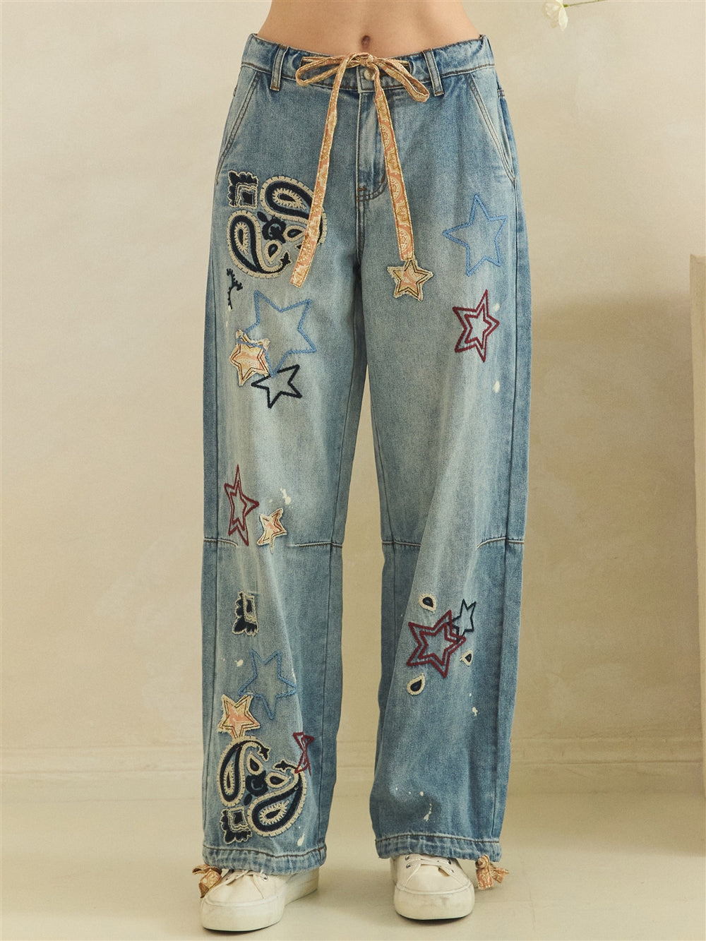 Front waist-to-hem view of washed blue jeans with stars, paisley embroidery and horizontal knee seams