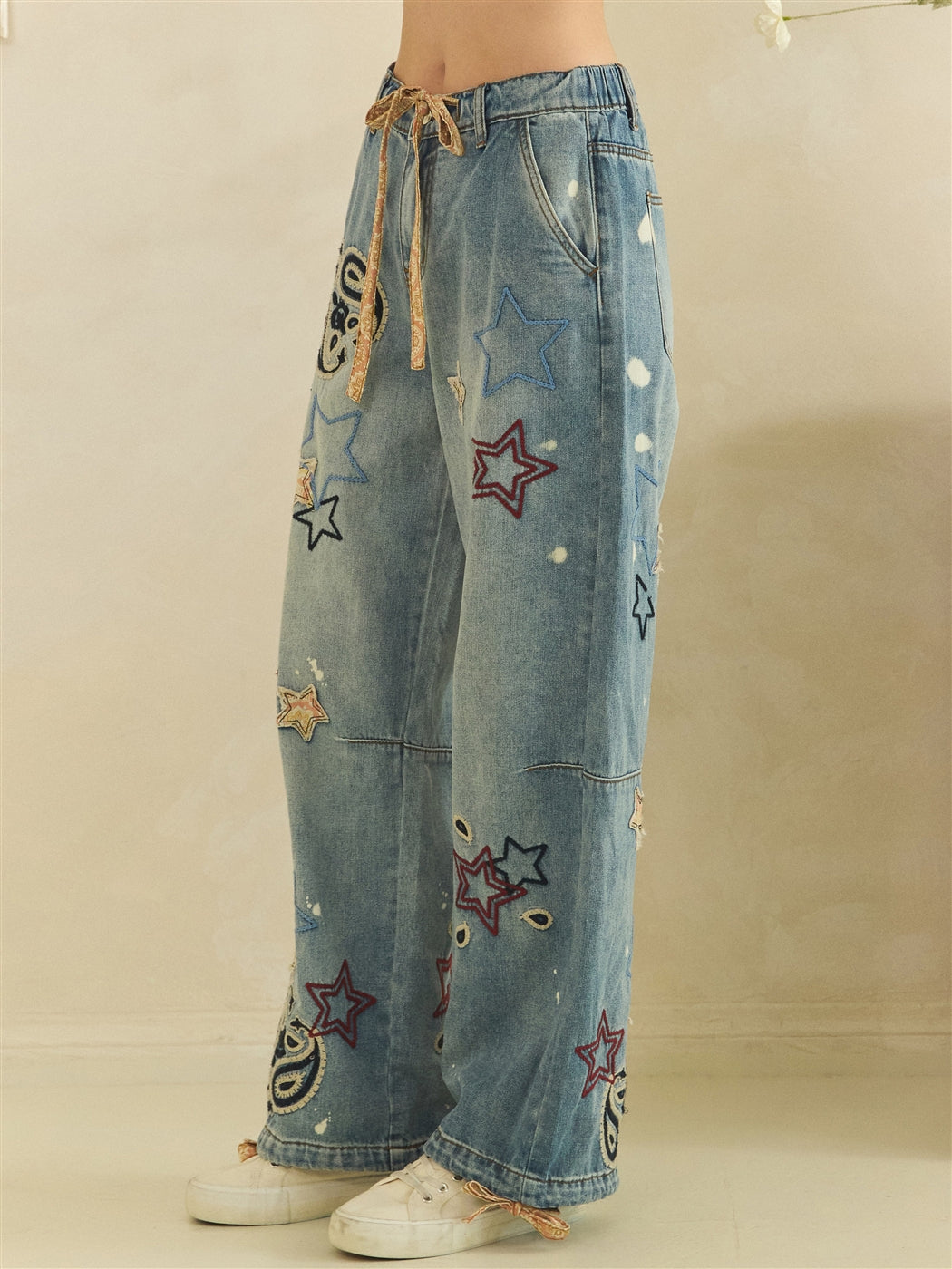 Angled view of blue wide-leg jeans showing outlined stars, faded spots and a tan waist drawstring