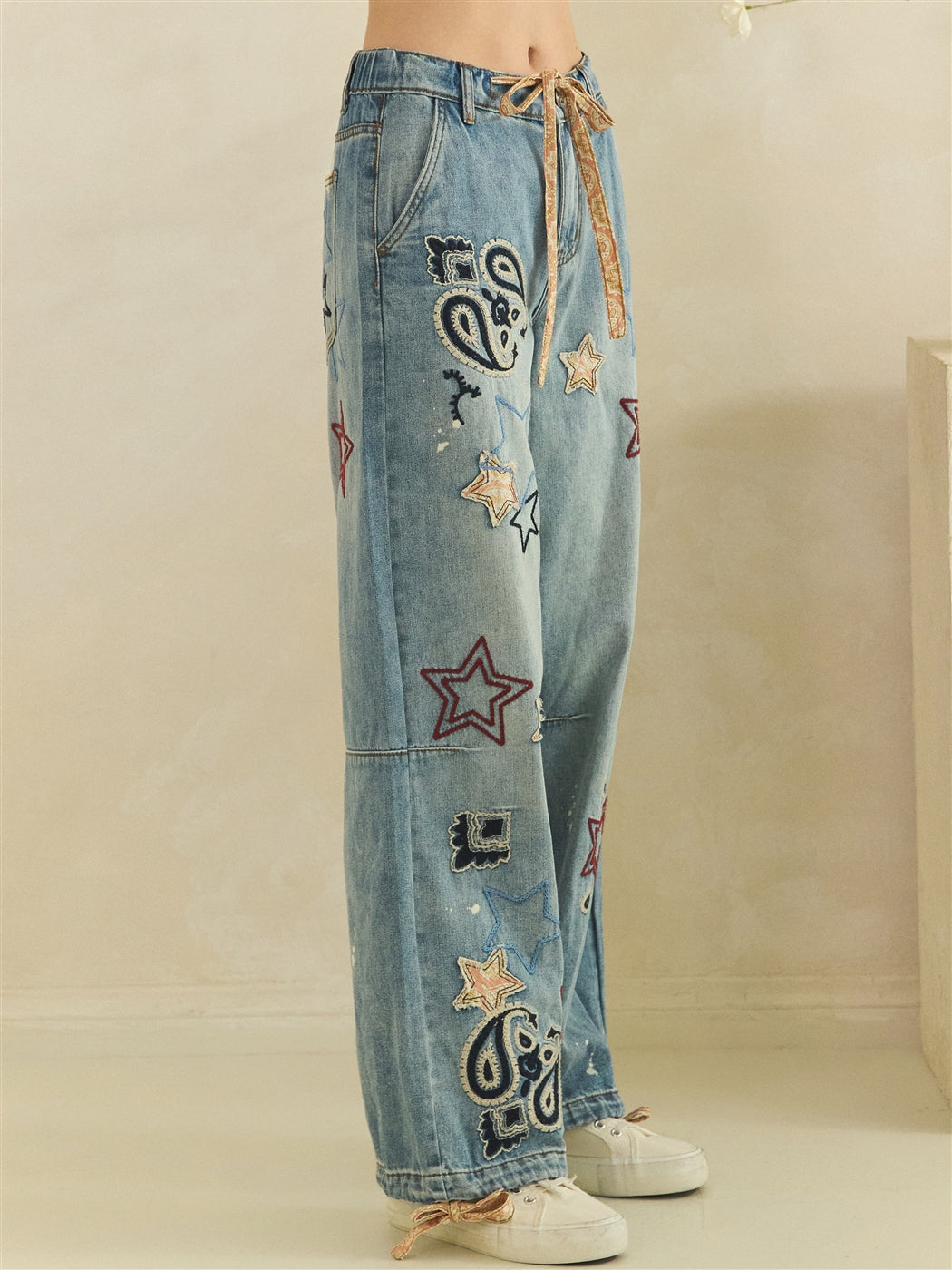 Side-front detail of blue embroidered jeans with a curved pocket and black and cream paisley motifs