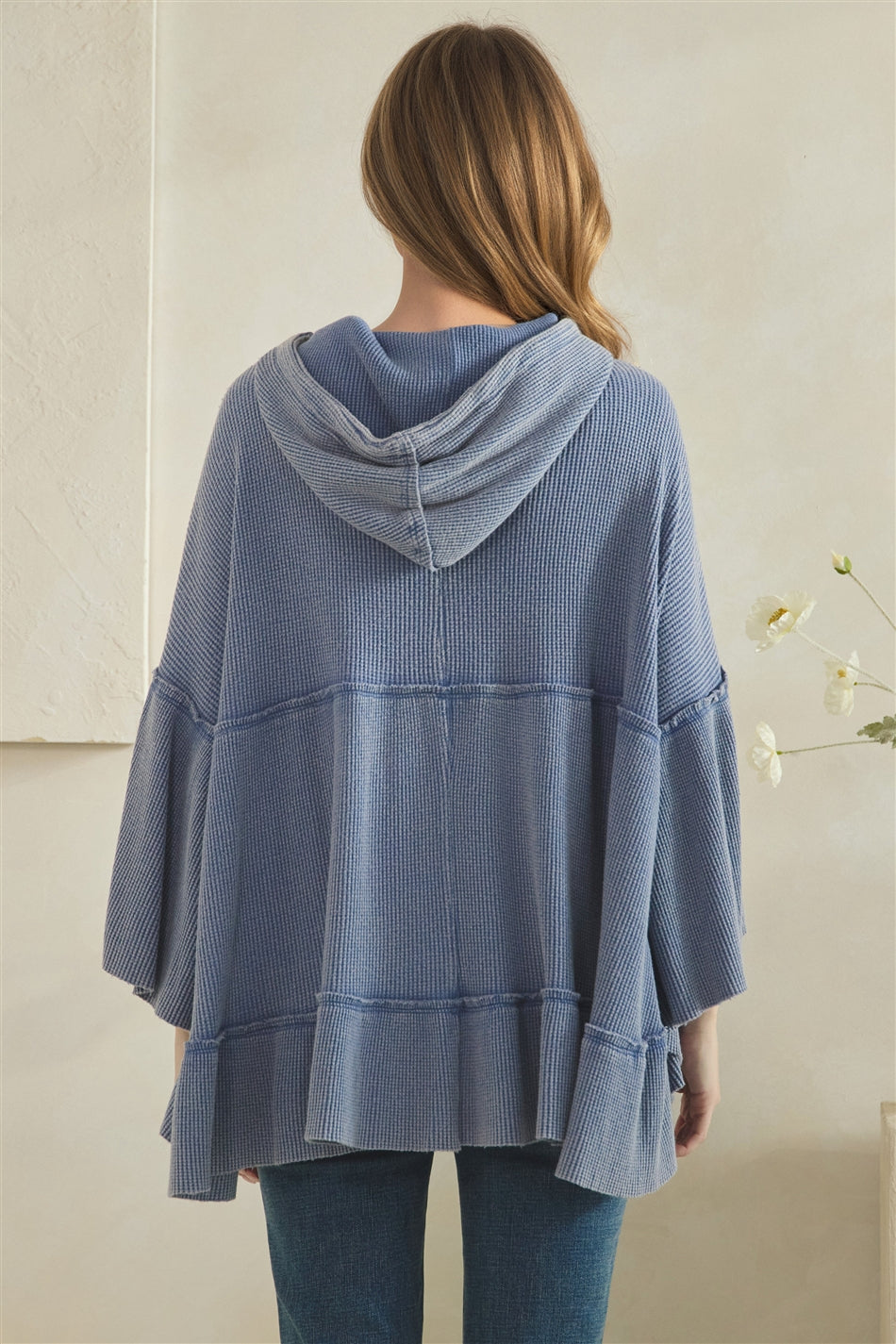 Back view of a light blue waffle hoodie with a draped hood, exposed seams and gathered lower hem