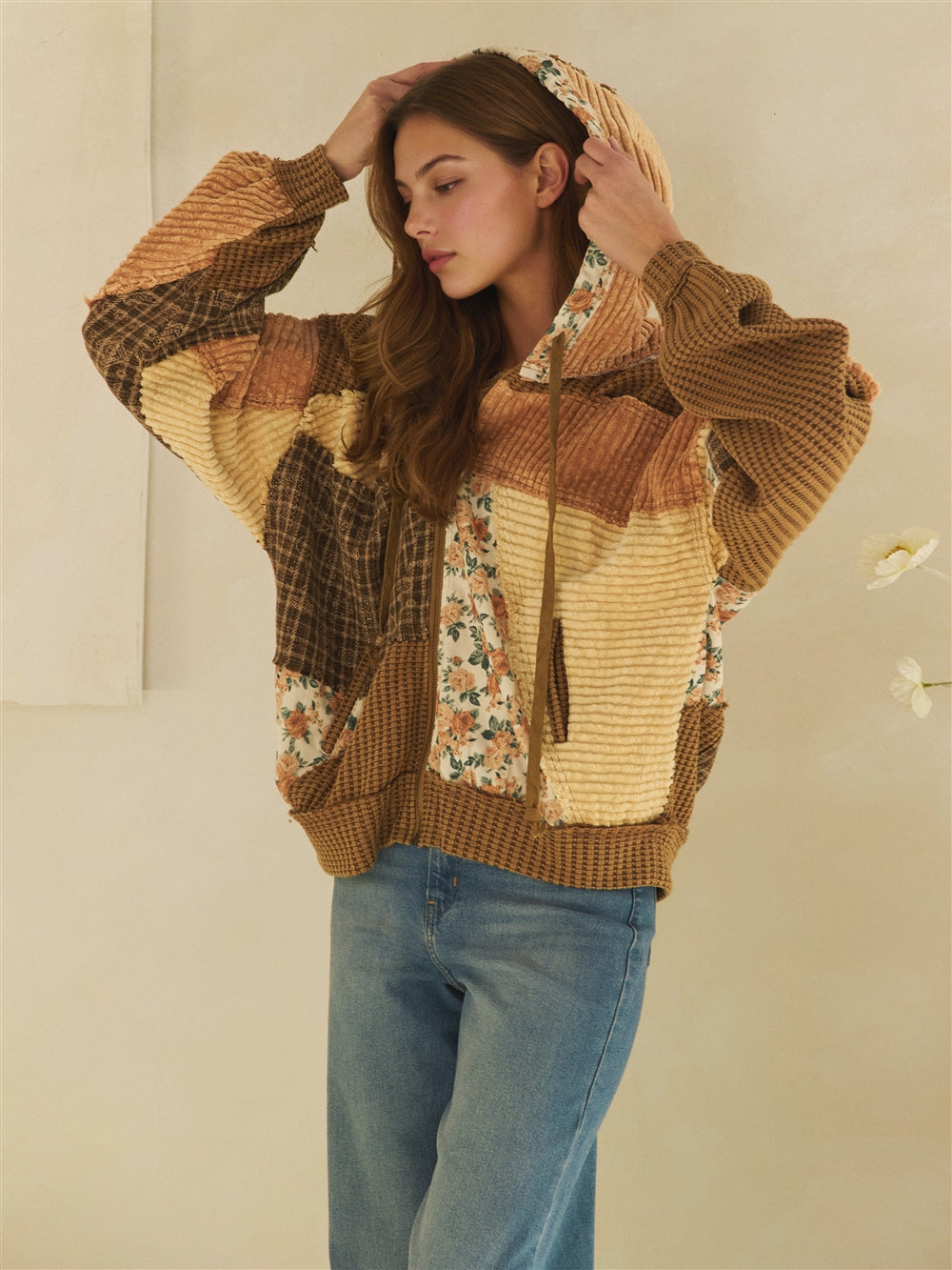 Front view of a brown patchwork hooded jacket worn open over a beige tank and blue jeans.