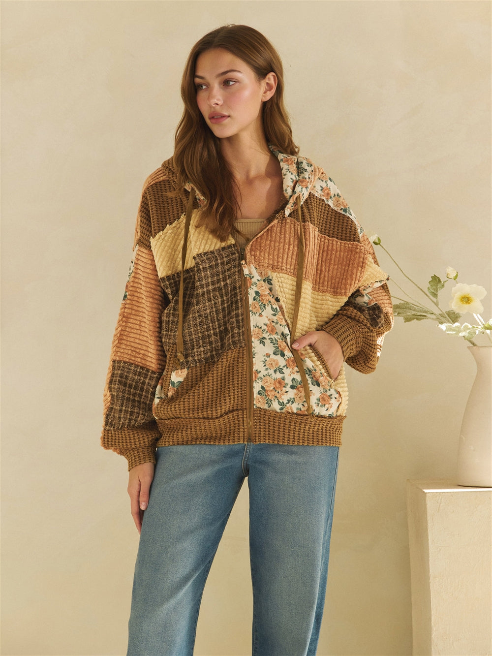 Brown floral and plaid patchwork jacket zipped at the front, styled with blue jeans.