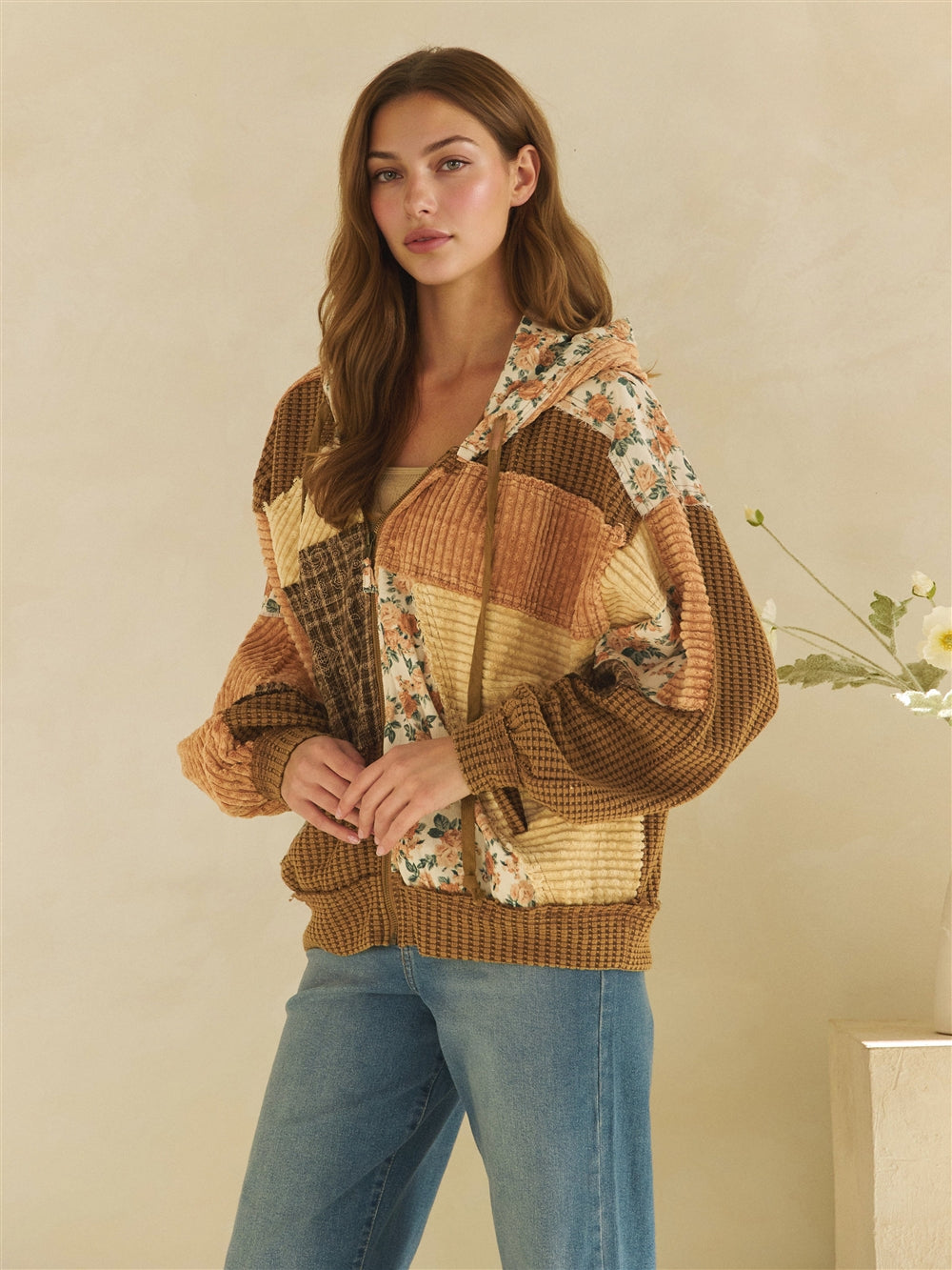 Woman lifting the hood of a brown mixed-texture patchwork jacket with floral and plaid panels.