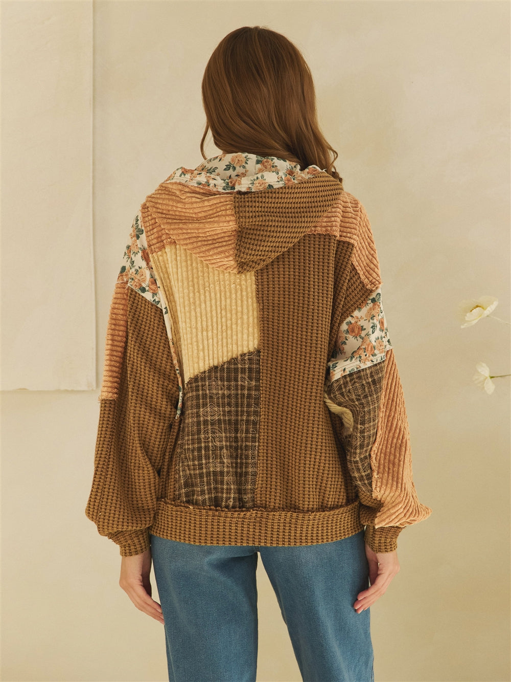 Three-quarter front view of a brown patchwork zip jacket with floral pockets and textured sleeves.